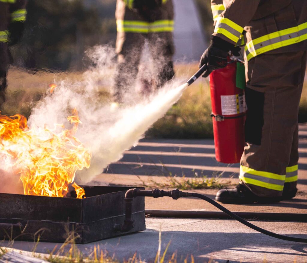 Firefighter putting out a controlled fire with a fire extinguisher during a training exercise